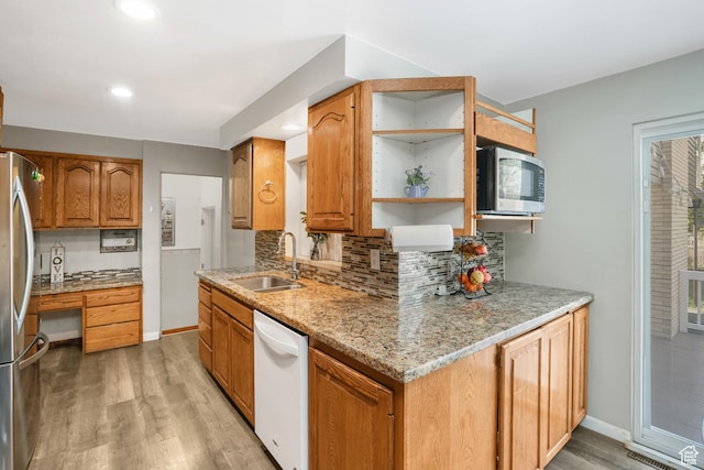 kitchen with light stone countertops, a sink, appliances with stainless steel finishes, decorative backsplash, and brown cabinetry