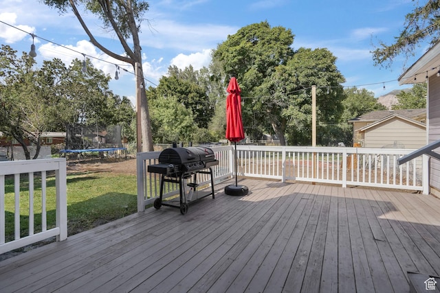 wooden deck with a trampoline, a yard, and area for grilling