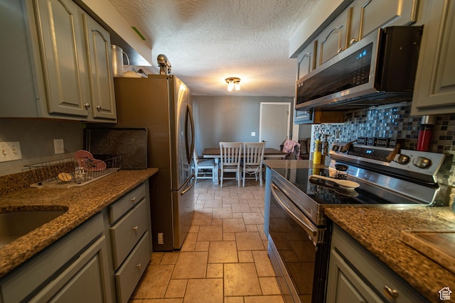 kitchen featuring gray cabinetry, stainless steel appliances, decorative backsplash, and stone tile floors