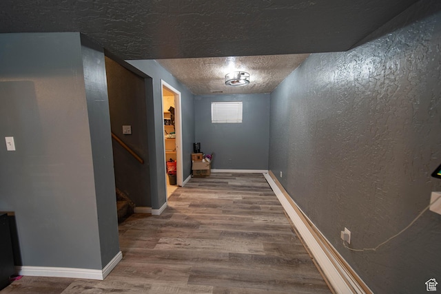 corridor featuring baseboards, a textured wall, wood finished floors, stairs, and a textured ceiling
