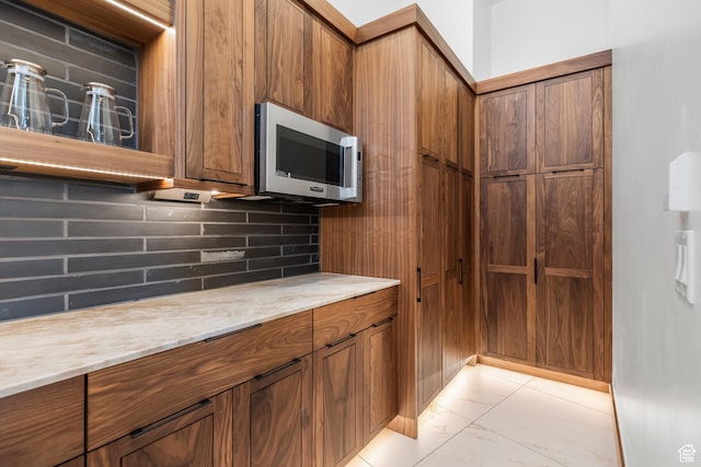 kitchen featuring marble finish floor, tasteful backsplash, stainless steel microwave, and brown cabinets