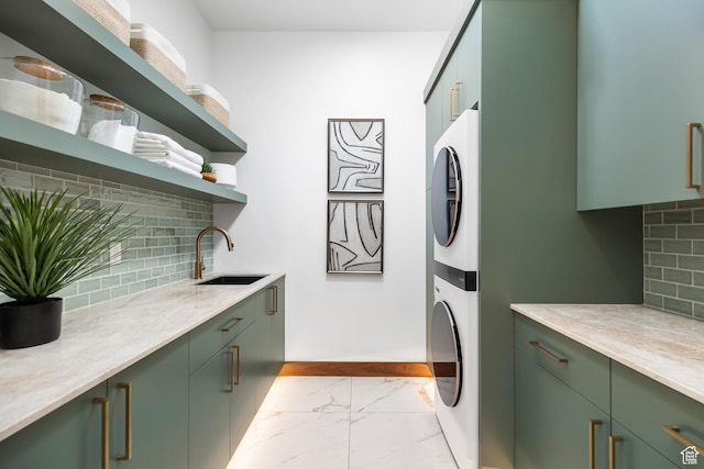 laundry area with stacked washer and dryer, a sink, baseboards, marble finish floor, and cabinet space