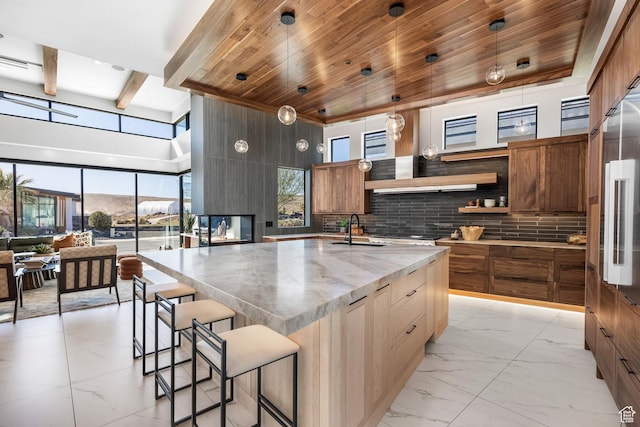kitchen with marble finish floor, hanging light fixtures, brown cabinetry, a sink, and an island with sink