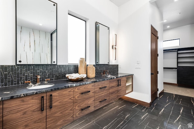 full bath with double vanity, backsplash, a walk in closet, and a sink