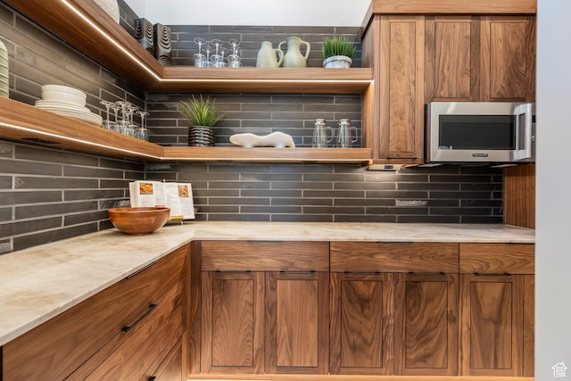 kitchen with brown cabinetry, light countertops, stainless steel microwave, and decorative backsplash