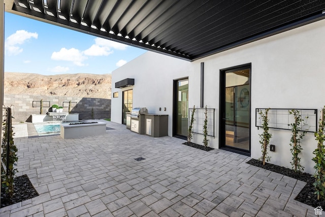view of patio featuring an outdoor fire pit, an outdoor kitchen, a mountain view, area for grilling, and fence
