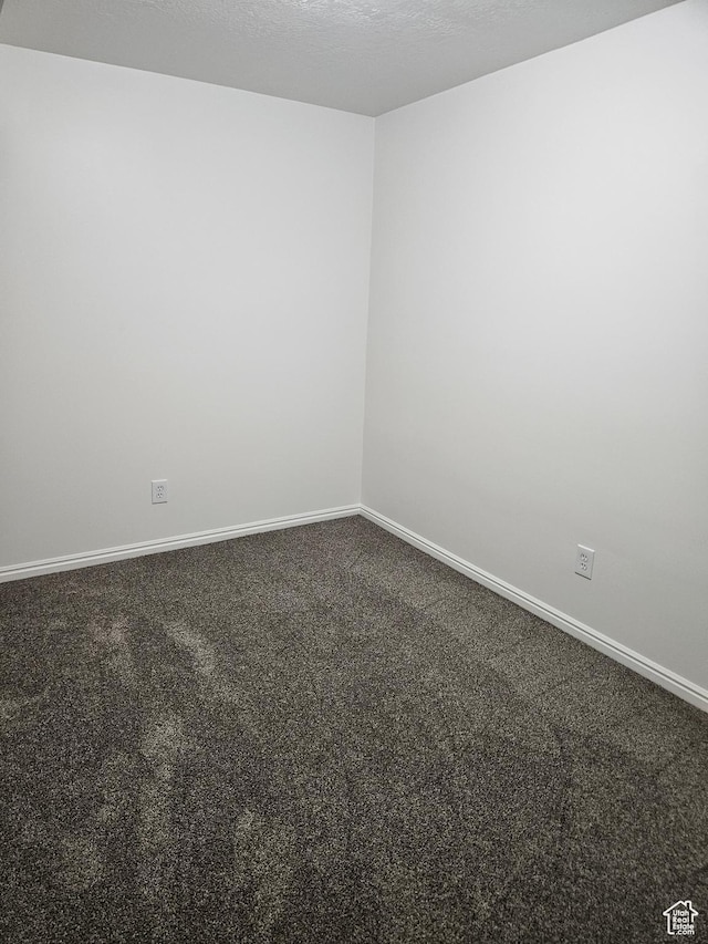 empty room with a textured ceiling, dark carpet, and baseboards