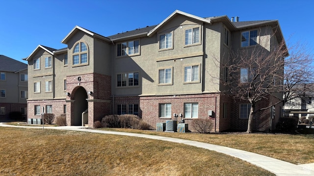 view of front of property featuring brick siding, central air condition unit, a front yard, and stucco siding