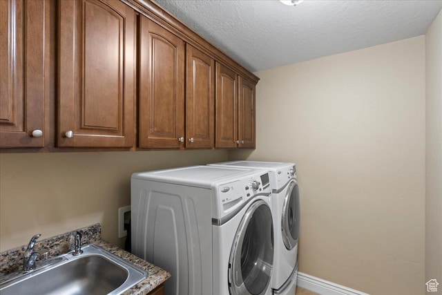 clothes washing area with cabinet space, baseboards, washing machine and clothes dryer, a textured ceiling, and a sink
