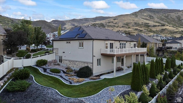 back of property featuring solar panels, a mountain view, a balcony, stone siding, and a fenced backyard