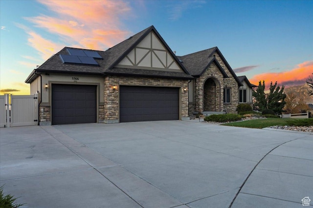 english style home with a garage, solar panels, driveway, a gate, and stucco siding