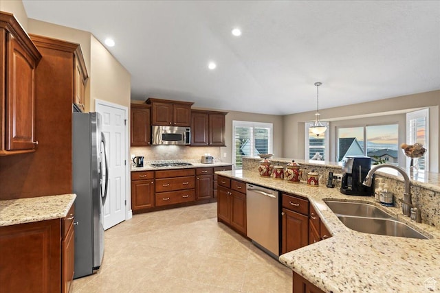 kitchen with decorative light fixtures, a sink, light stone countertops, stainless steel appliances, and backsplash