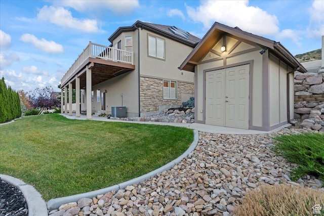 rear view of house with an outdoor structure, stone siding, a lawn, a wooden deck, and stucco siding
