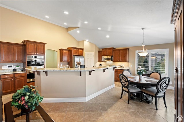 kitchen featuring light stone counters, decorative light fixtures, a center island with sink, a breakfast bar area, and appliances with stainless steel finishes