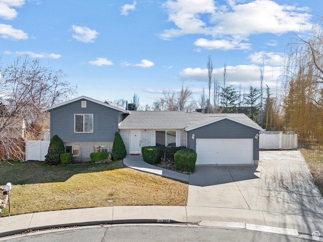 tri-level home featuring driveway, a garage, brick siding, fence, and a front yard