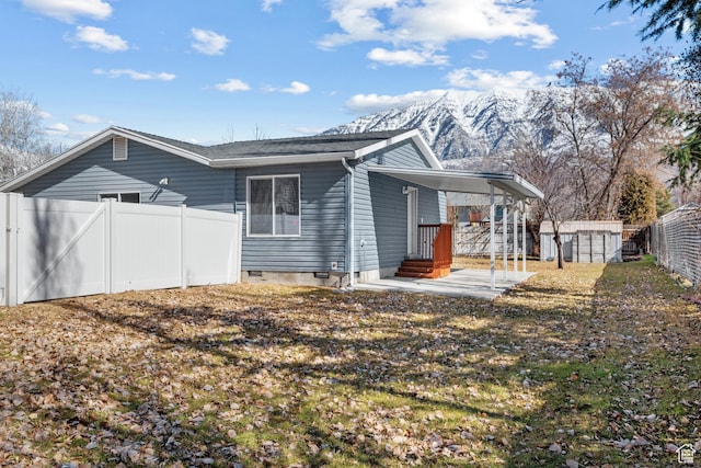back of house featuring a storage shed, a fenced backyard, an attached carport, crawl space, and a mountain view