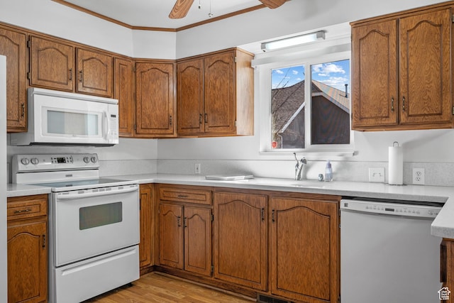 kitchen with brown cabinets, white appliances, light countertops, and crown molding