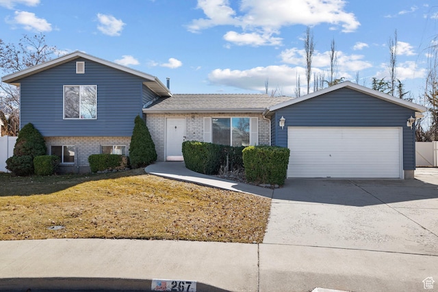split level home featuring a garage, brick siding, and driveway