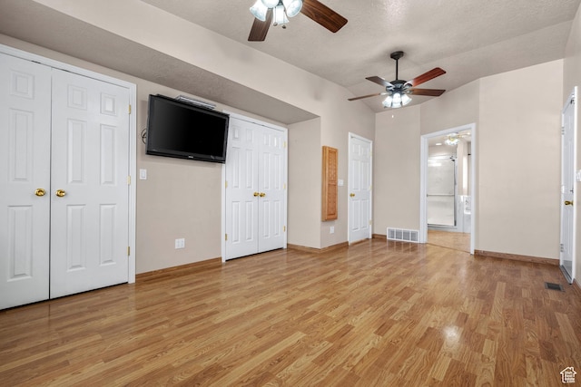 unfurnished bedroom featuring vaulted ceiling, light wood finished floors, two closets, and visible vents