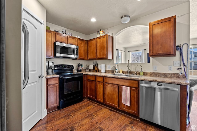 kitchen featuring a textured ceiling, dark wood-type flooring, a sink, appliances with stainless steel finishes, and brown cabinets