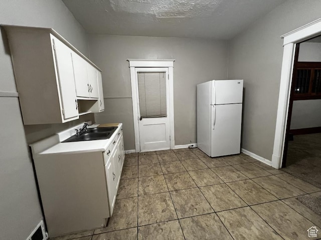 kitchen featuring light countertops, freestanding refrigerator, white cabinets, a sink, and baseboards