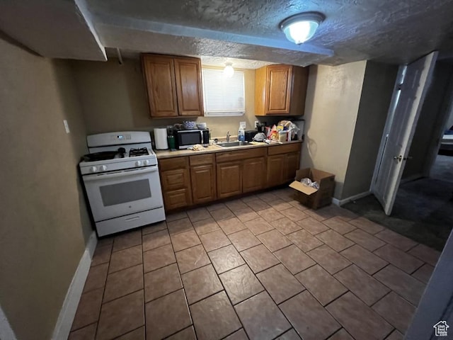 kitchen with light countertops, stainless steel microwave, a sink, a textured ceiling, and white range with gas stovetop