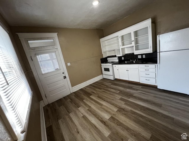 kitchen with white appliances, dark countertops, glass insert cabinets, white cabinetry, and a sink