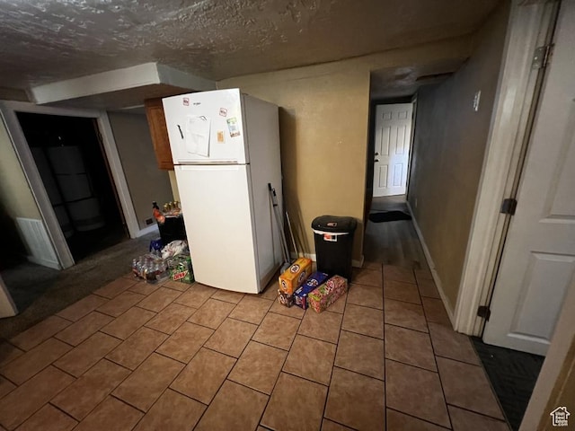 interior space featuring a textured ceiling, tile patterned flooring, freestanding refrigerator, and baseboards