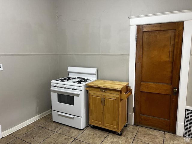 kitchen featuring light tile patterned floors, butcher block countertops, white gas range, and brown cabinets