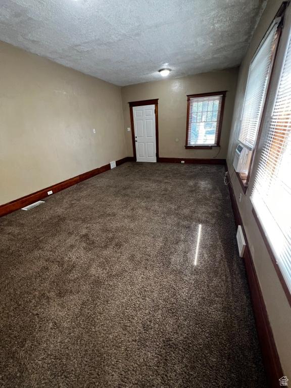 empty room featuring baseboards, visible vents, cooling unit, a textured ceiling, and dark carpet