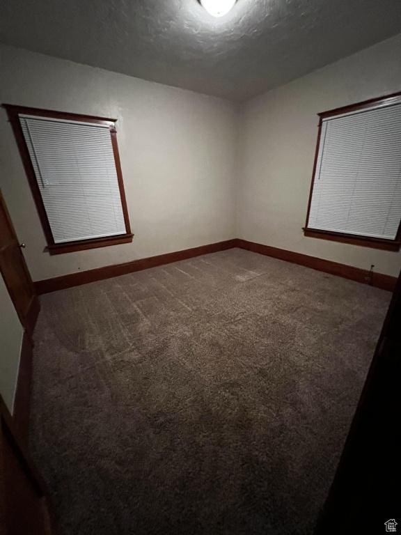 carpeted spare room featuring a textured ceiling and baseboards