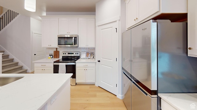 kitchen with light stone countertops, white cabinets, appliances with stainless steel finishes, decorative backsplash, and light wood finished floors
