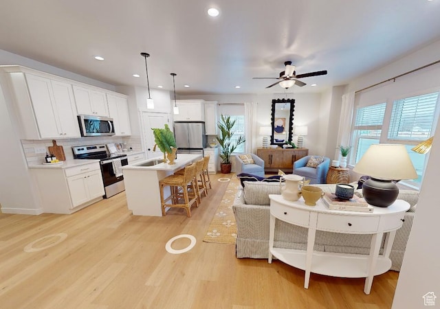 kitchen featuring an island with sink, open floor plan, decorative light fixtures, stainless steel appliances, and light countertops