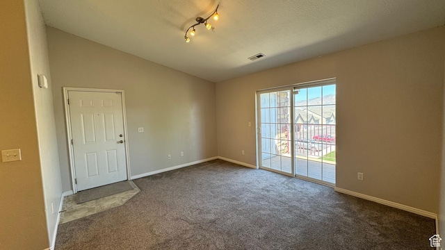 spare room with dark colored carpet, vaulted ceiling, and baseboards