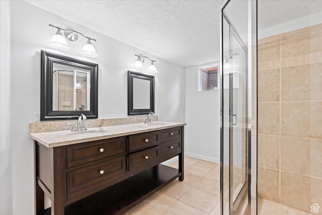 full bathroom with double vanity, a textured ceiling, a shower stall, and a sink