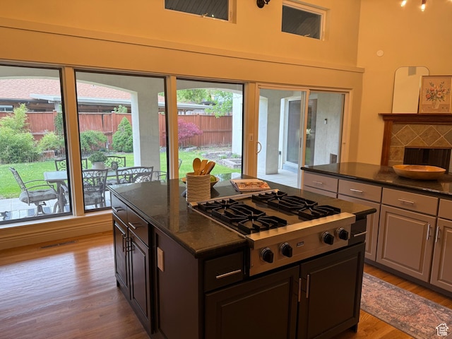 2765 E Blue Spruce Dr, Holladay, UT 84117 - kitchen with stainless steel gas stovetop, light wood-type flooring, a kitchen island, dark stone counters, and a towering ceiling