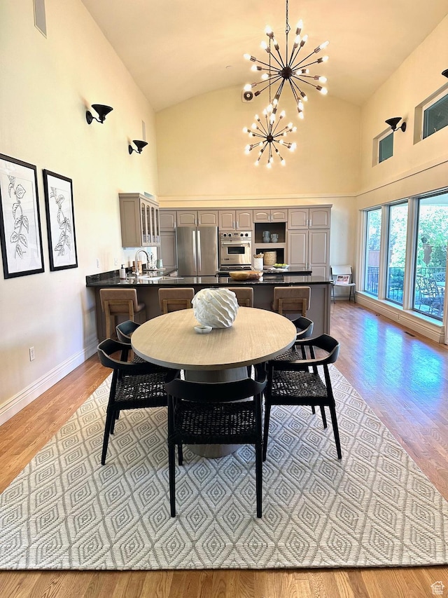 dining area with light wood-type flooring, high vaulted ceiling, baseboards, visible vents, and a notable chandelier
