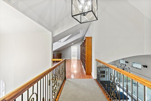corridor with high vaulted ceiling, wood finished floors, a healthy amount of sunlight, and a notable chandelier