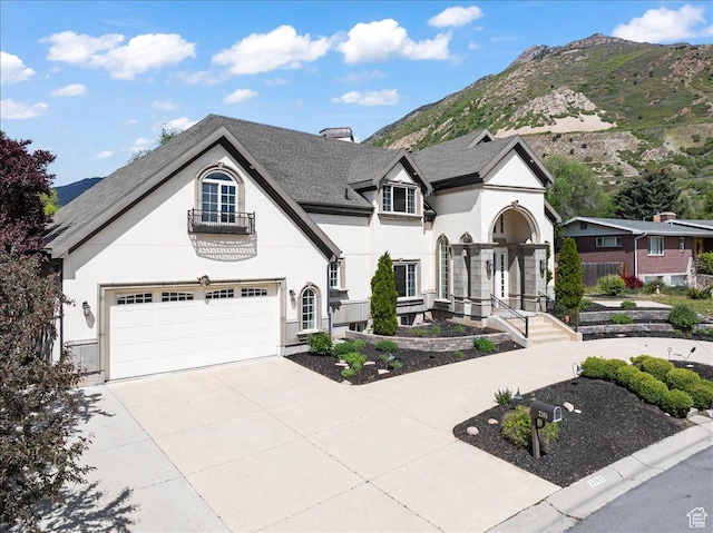 french country style house with a balcony, stucco siding, a mountain view, and driveway