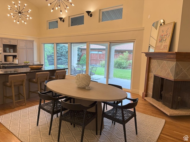 dining area with an inviting chandelier, a tiled fireplace, light wood-style flooring, and high vaulted ceiling