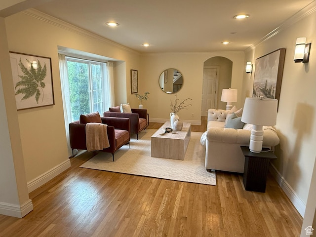 living room featuring arched walkways, light wood-style floors, ornamental molding, and baseboards