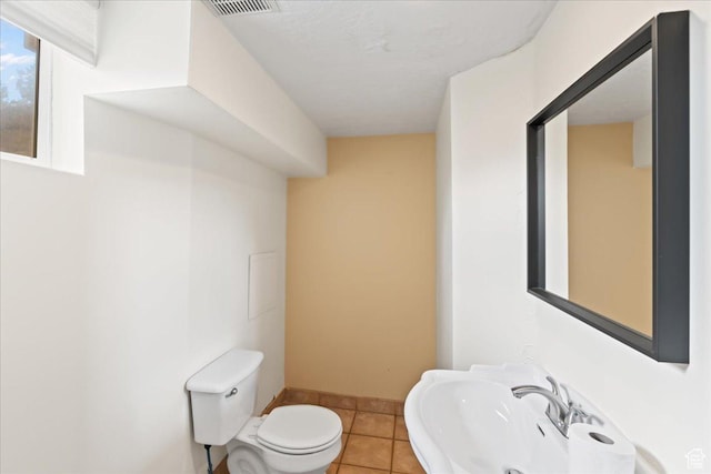 half bathroom featuring a sink, tile patterned flooring, toilet, and baseboards