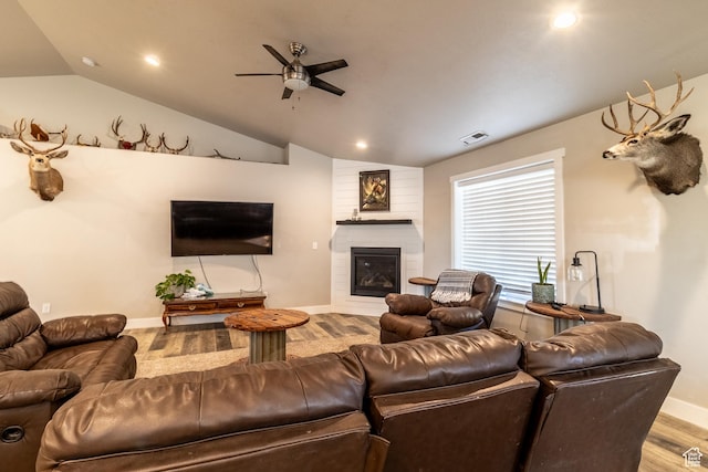 living area featuring a fireplace, visible vents, vaulted ceiling, and wood finished floors