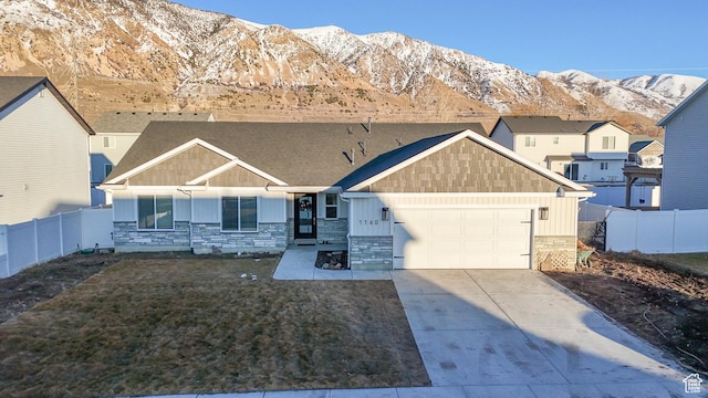 view of front of property featuring a garage, driveway, stone siding, fence, and a mountain view