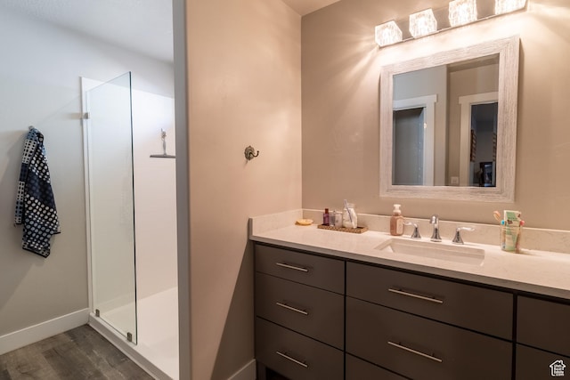 full bath featuring a stall shower, vanity, baseboards, and wood finished floors