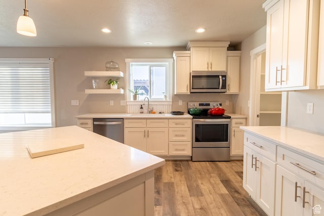 kitchen featuring light stone counters, hanging light fixtures, appliances with stainless steel finishes, white cabinetry, and a sink