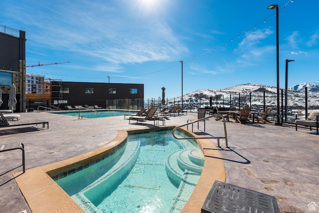 snow covered pool featuring a mountain view, fence, a community pool, and a patio