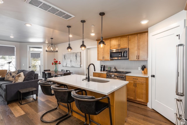 kitchen featuring decorative light fixtures, a center island with sink, light countertops, appliances with stainless steel finishes, and a sink
