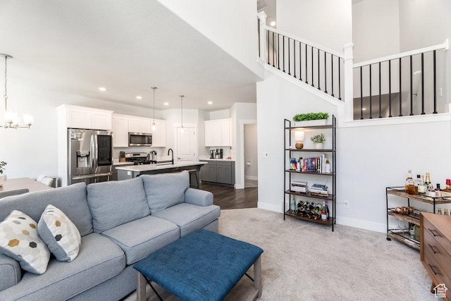carpeted living room featuring a chandelier, stairway, a sink, and baseboards