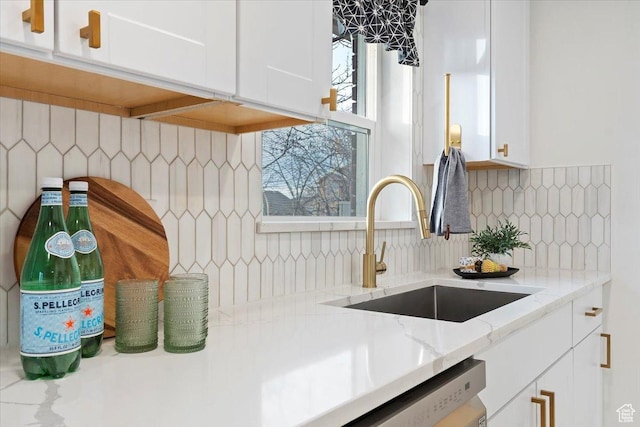 kitchen with light stone counters, a sink, white cabinetry, stainless steel dishwasher, and tasteful backsplash